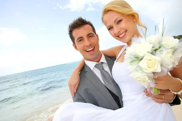 Sposo che tiene sposa tra le braccia in spiaggia — Foto Stock