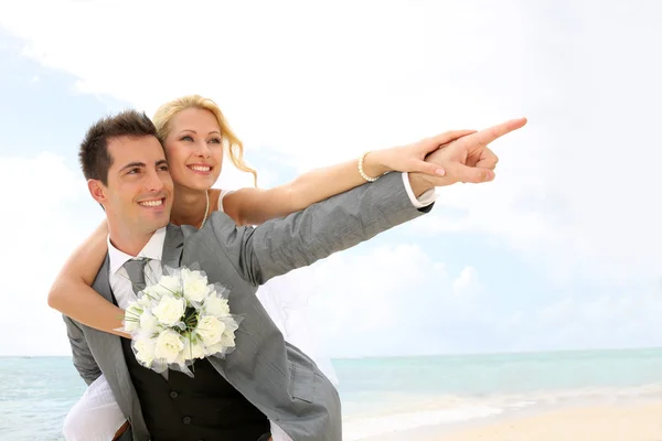 Huwelijksreis piggyback ritje op het strand — Stockfoto