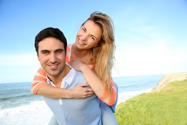 Hombre dando paseo a cuestas a su novia junto al mar — Foto de Stock