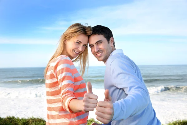 Casal mostrando polegares para cima em frente ao mar — Fotografia de Stock