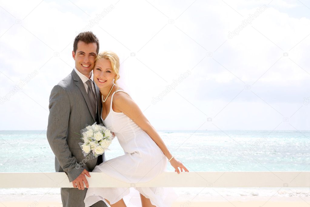 Bride and groom sitting on a fence by the beach