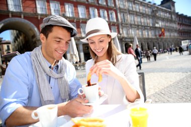 Cheerful couple of tourists eating churros in Madrid clipart