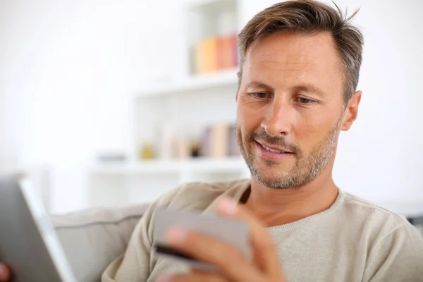 Bonito homem sorridente em casa comprando na internet — Fotografia de Stock