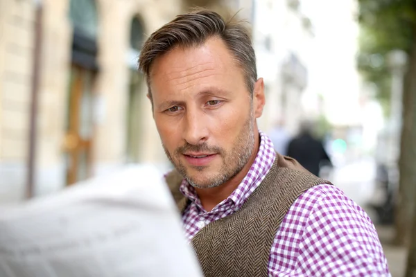 Man reading newspaper on a public bench — Stock Photo, Image