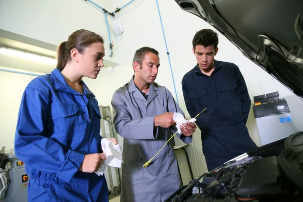 Instructor con estudiantes en taller de reparación cambiando aceite de motor —  Fotos de Stock