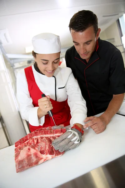 Butcher teaching student with meat cutting — Stock Photo, Image