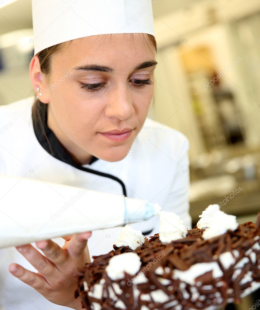 Pastry cook putting whipped cream on cake