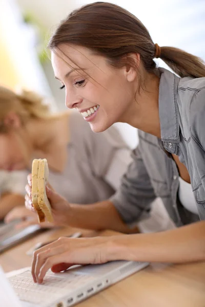 Chica comiendo sándwich en frente de la computadora portátil —  Fotos de Stock
