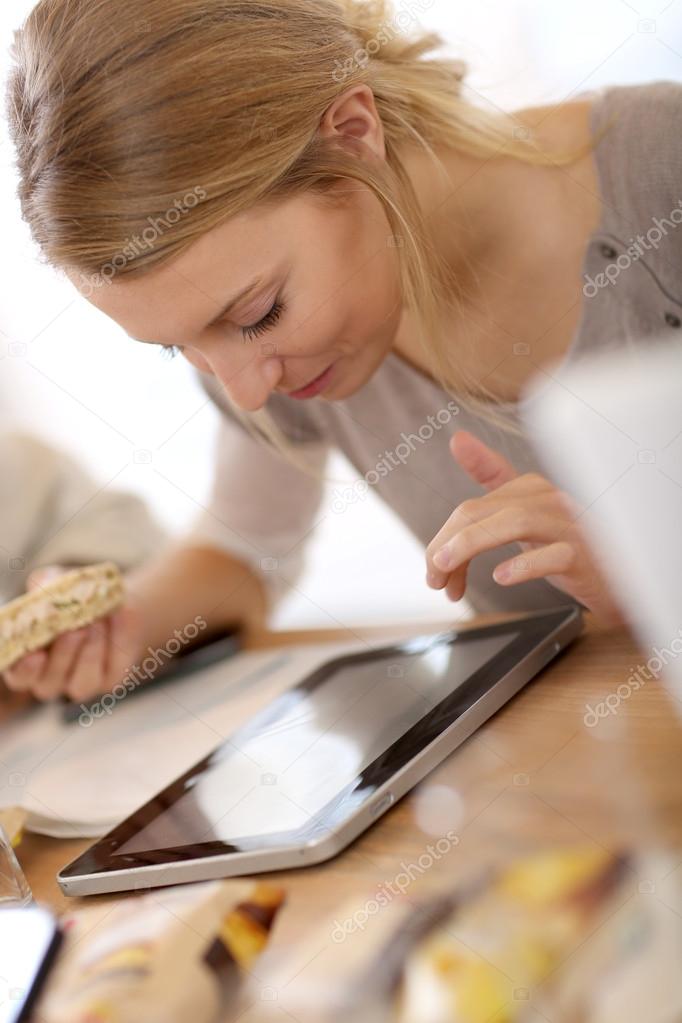 Woman at work eating sandwich and using tablet