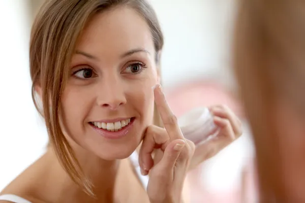 Chica poniendo crema anti-envejecimiento en su cara —  Fotos de Stock