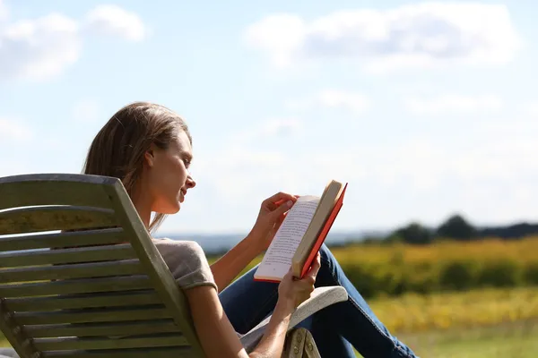 Frau liest Buch im langen Stuhl — Stockfoto