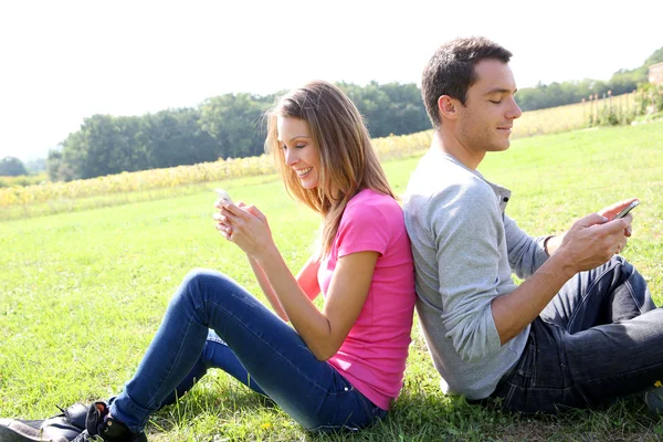 Coppia in campo che gioca con smartphone Foto Stock