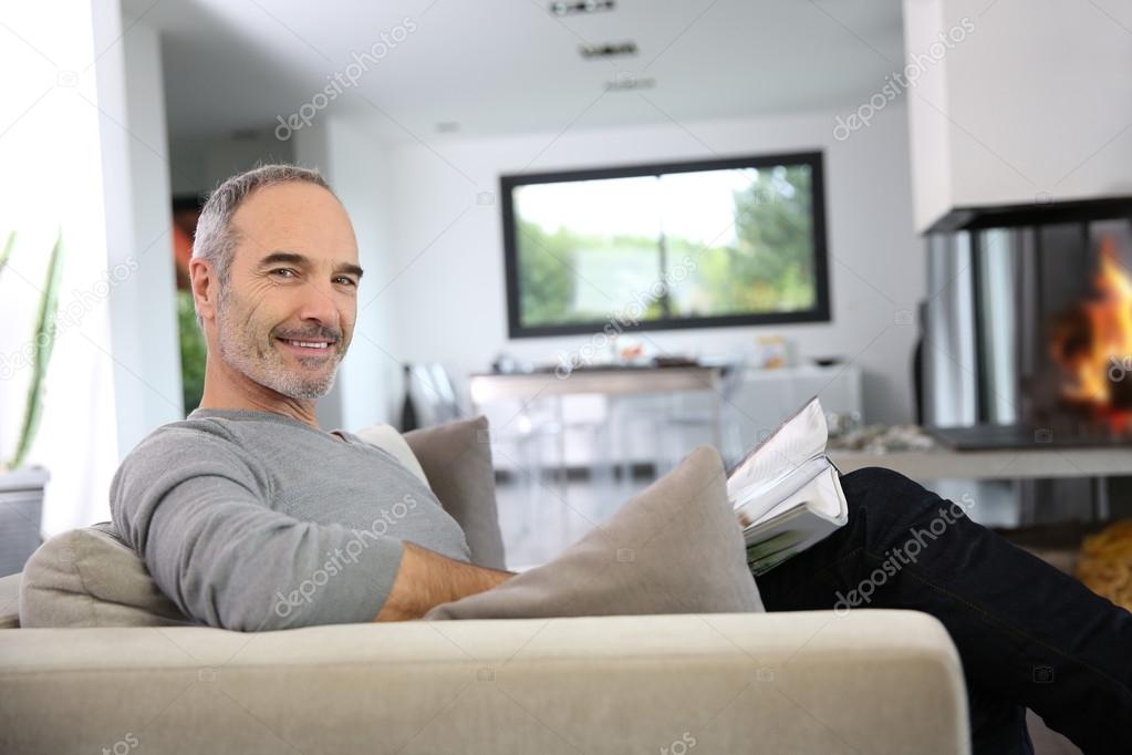 Man reading newspaper by fireplace