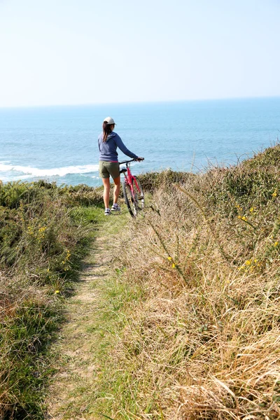 Girl riding bicycle by ocean coastline — Stock Photo, Image