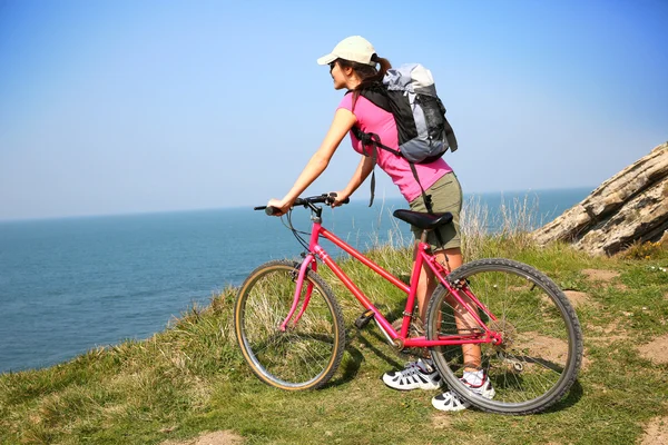 Woman riding bike by ocean coast — Stock Photo, Image