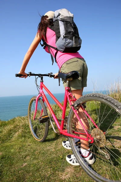 Woman riding bike by ocean coast — Stock Photo, Image