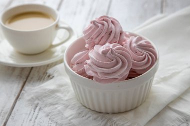 Beyaz ahşap bir masada beyaz bir kasede pembe kremalı şekerlemeler..