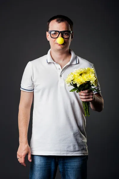 Retrato de cara com nariz amarelo engraçado segurando monte de flores — Fotografia de Stock