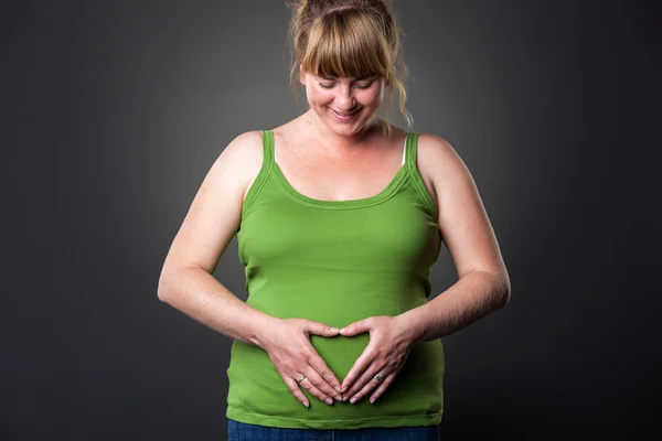 Glückliche junge prängante Frau im Studio - dunkler Hintergrund — Stockfoto