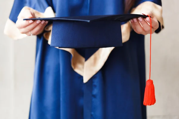 Jovem estudante segurando chapéu acadêmico nas mãos — Fotografia de Stock