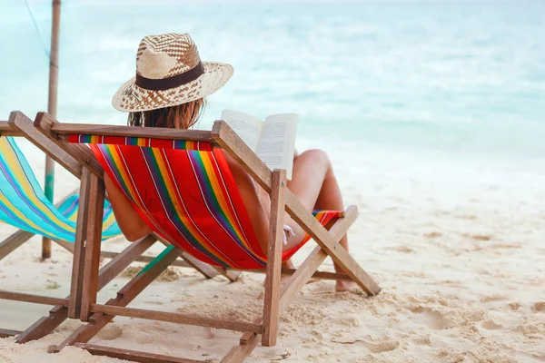 Ung vacker kvinna som sitter på stranden, läsa en bok Stockfoto