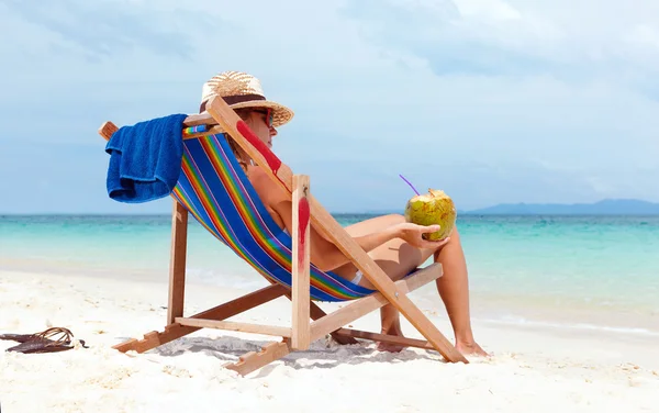 Junge Frau mit Hut sitzt am tropischen Strand — Stockfoto