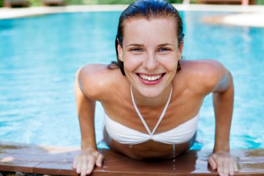 Tropik tatil köyünde havuz başında poz veren güzel genç bir kadın.