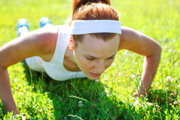 Young woman doing push ups on green grass.