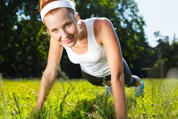 Mujer joven haciendo flexiones en la hierba verde . — Foto de Stock