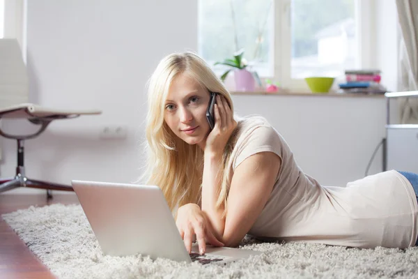 Mulher usando laptop e telefone no tapete — Fotografia de Stock