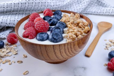 Bir porsiyon yoğurt, yabanmersinli ahududu ve ahşap bir kasede servis edilmeye hazır yulaf gevreği. Diyet konsepti için sağlıklı yiyecekler. Yoğurtlu meyveli müsli..