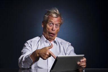 Shocked senior man pointing to his tablet clipart