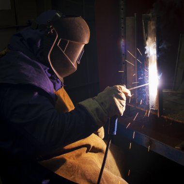 Metal ve kıvılcımlar üreten koruyucu maskeli kaynakçı.