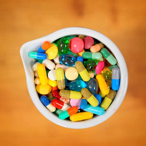 Bowl of multicolored tablets and capsules — Stock Photo, Image