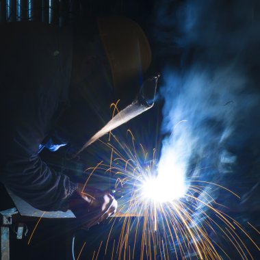 Metal ve kıvılcımlar üreten koruyucu maskeli kaynakçı.