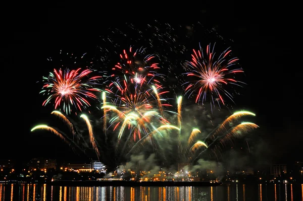 Fuochi d'artificio sulla città di notte con riflesso in acqua — Foto Stock