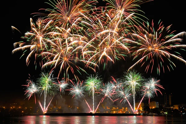 Fogos de artifício sobre a cidade à noite com reflexão na água — Fotografia de Stock