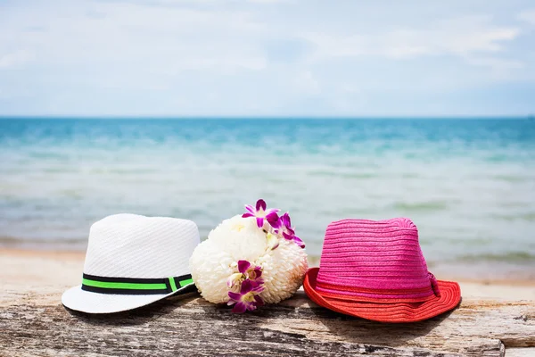 Twee hoeden en bloemen op een strand — Stockfoto