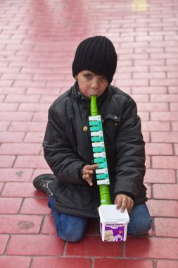 STANBUL, TURKEY - MARCH 9, 2014 : Little kid playing a plastic flute in the street, collecting money from people walking by. Working kids issue is an important problem in Istanbul, taken on March 9 clipart