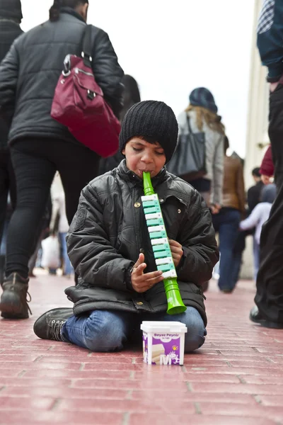 STANBUL, TURKEY - MARCH 9, 2014 : Little kid playing a plastic flute in the street, collecting money from people walking by. Working kids issue is an important problem in Istanbul, taken on March 9 — Stock Photo, Image
