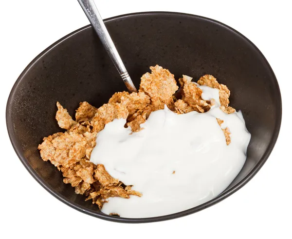 Yoghurt and spoon into bowl of cereal — Stock Photo, Image