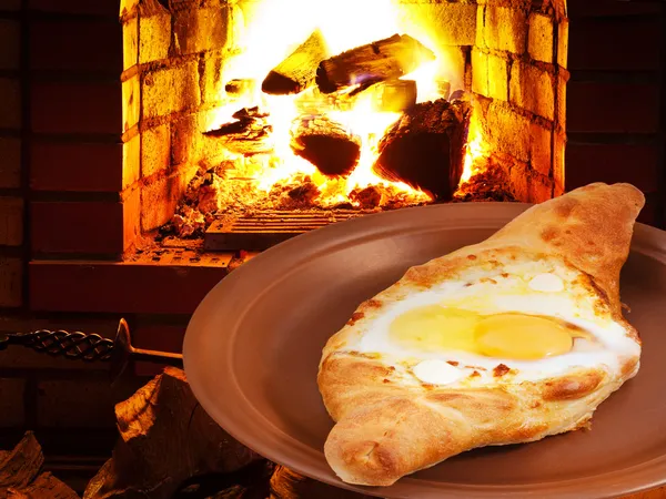 Hachapuri with egg on plate and fire in stove — Stock Photo, Image