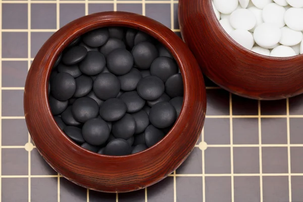 Black go stones in wooden bowl on go board — Stock Photo, Image
