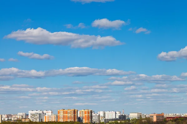 Valkoiset pilvet sinisellä taivaalla kaupunkialueen yllä — kuvapankkivalokuva