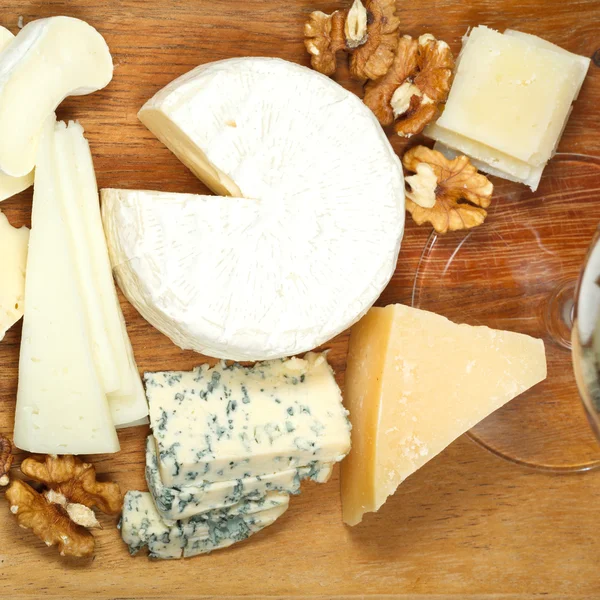 Glass and assortment of cheeses on wooden plate — Stock Photo, Image