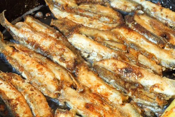 Fried fish capelin on black frying pan — Stock Photo, Image