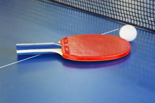 Remo vermelho, bola de tênis na mesa de ping pong azul — Fotografia de Stock