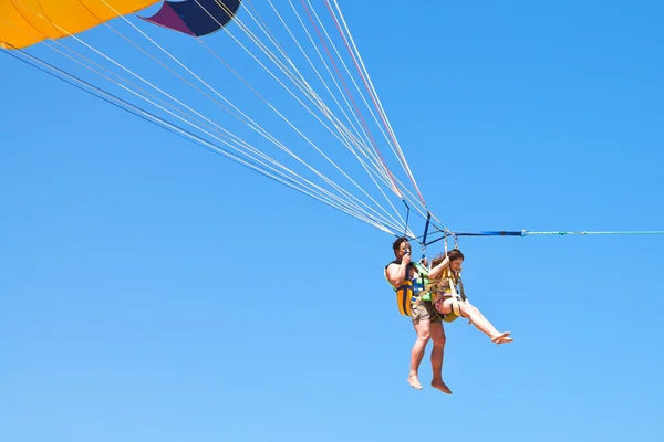 Man en meisje parasailen op parachute in blauwe hemel — Stockfoto