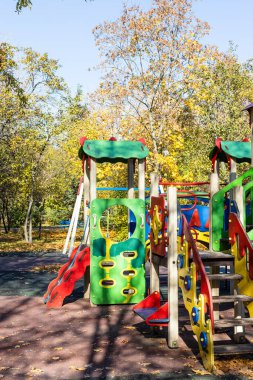Güneşli bir sonbahar gününde şehir parkındaki çocuk parkında renkli ahşap binişler, slaytlar ve evler.