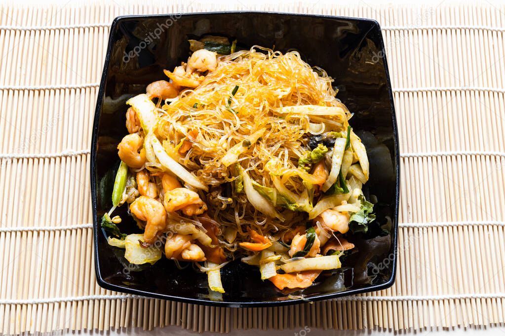 portion of Mien Xao Vietnamese wok stir-fried glass noodles with vegatables and prawns in black bowl on wooden table